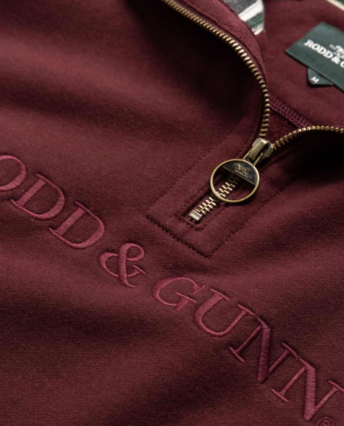 The Rodd & Gunn Alford Forest Sweat is a maroon mid-weight jersey quarter-zip sweatshirt, featuring an embossed logo on the chest and a circular pull tab zipper, with a small branded tag near the collar.
