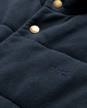 Close-up of the Rodd & Gunn Lake Ferry Vest, a textured dark fabric vest with gold buttons, a small embroidered dog logo in dark blue, crafted from USA Cotton for lightweight insulation.