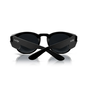 A pair of SafeStyle Cruisers matte black frame sunglasses with dark, polarised lenses, viewed from the back with the arms crossed. The brand name "SubStyle" is written in white on both arms. The sunglasses are positioned on a reflective white surface.