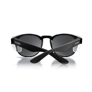 The folded SafeStyle Cruisers boast a black frame and tinted lenses with UV protection. A white script logo adorns the arms near the hinges, and they are displayed on a reflective white surface.