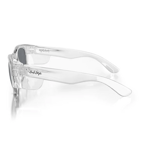 SafeStyle Classics Clear Frame Tinted Lens sunglasses feature thick clear frames and gray tinted lenses, resting on a white reflective surface. Subtle etching details the hinge, and the brand logo appears on the temple. Offering UV protection, their design is sleek and minimalist.