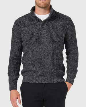 Wearing a Blazer Oscar Button Neck Knit in dark gray, a person stands against a light gray background with one hand in the pocket of their dark pants.
