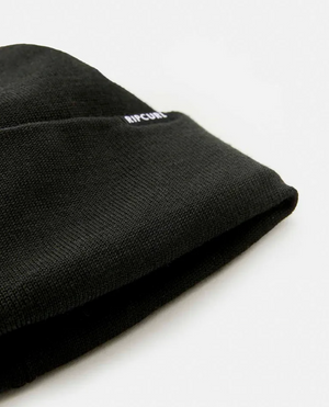 A close-up of the Rip Curl Anti-Series Regular Beanie against a white background. The textured black knit fabric adds depth, with "RIP CURL" subtly printed in small white letters near the edge, promising style and warmth.