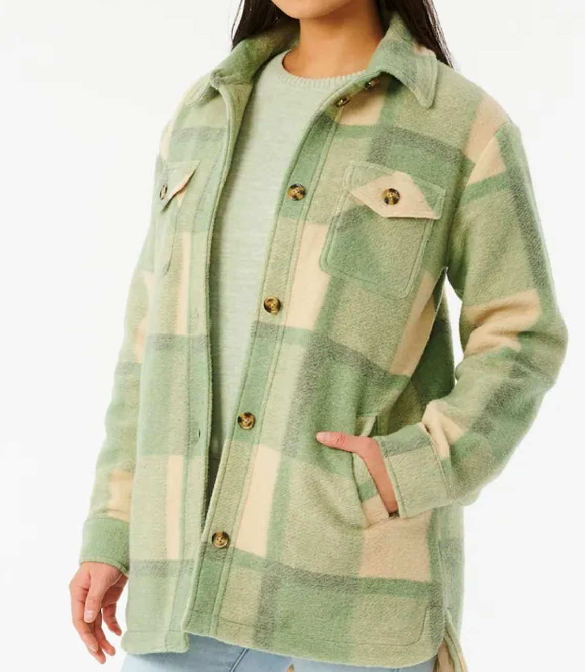 A person wears the Rip Curl Maniciana Jacket, a stylish light green and beige plaid design with buttons, over a green shirt. Featuring chest pockets and quilted lining, they comfortably tuck one hand in a side pocket against a plain white background.