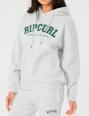 A person is dressed in a comfortable and casual Rip Curl Varsity Hoodie, which is fleece-lined with a gray relax fit and drawstring. "Ripcurl" is printed in green on both the chest of the hoodie and matching sweatpants.