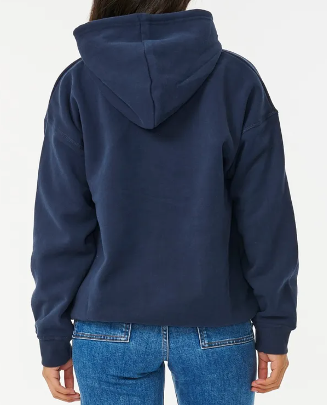 Rear view of a person in a cozy, dark blue Rip Curl Varsity Hoodie with the hood up and paired with blue jeans against a crisp white background.