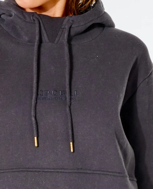 A person dons the Rip Curl Premium Surf Hoodie in dark gray, showcasing comfort with a front pocket and drawstrings. Subtle chest embroidery enhances its relaxed fit, contributing to the effortless style against a plain white background.