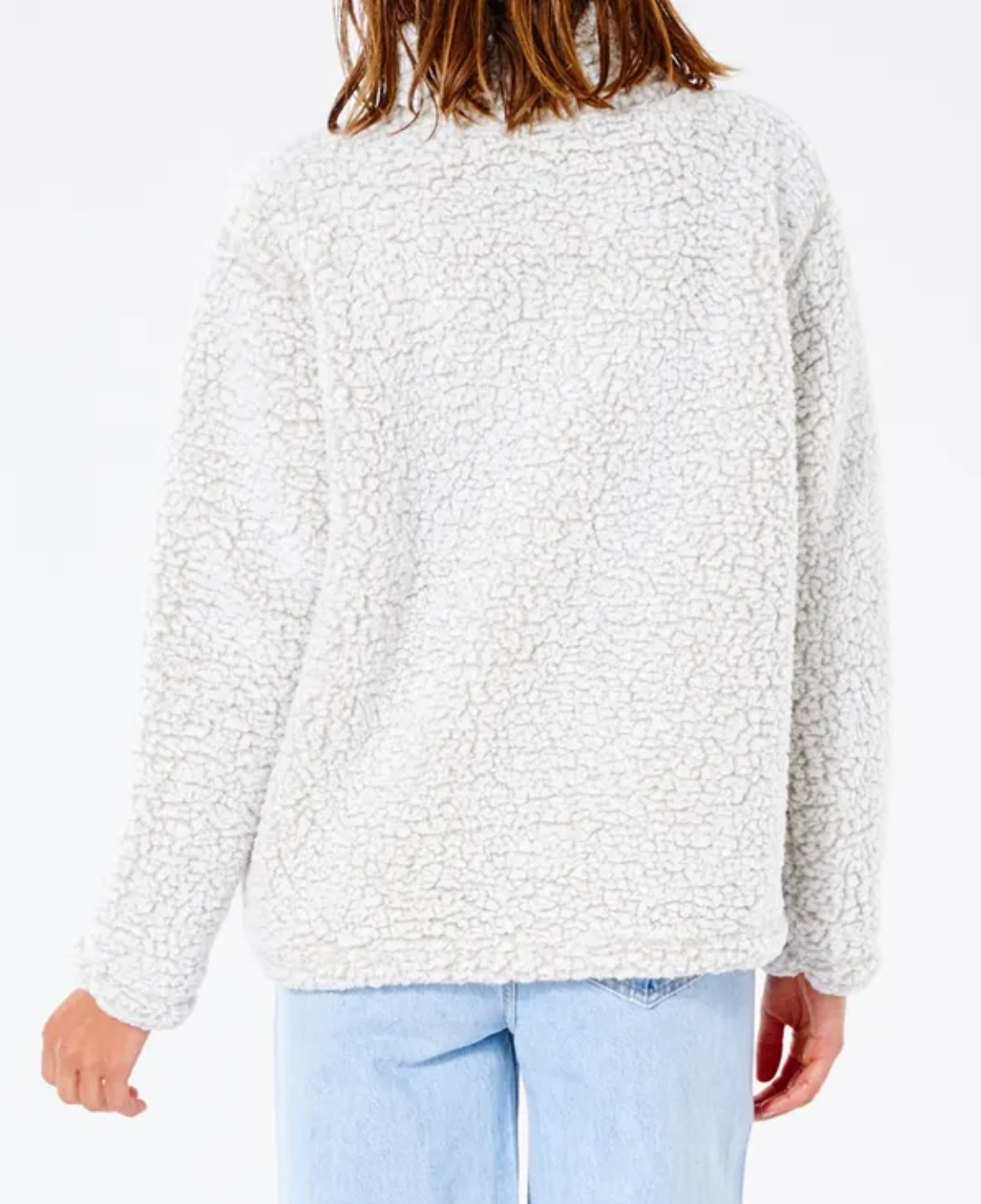 A person with long hair, turned away from the camera and one arm slightly bent, is wearing a Rip Curl Dark N Stormy 1/4 Zip Crew in light grey. The jacket is super soft fleece sherpa and has a textured appearance, paired with light blue jeans.