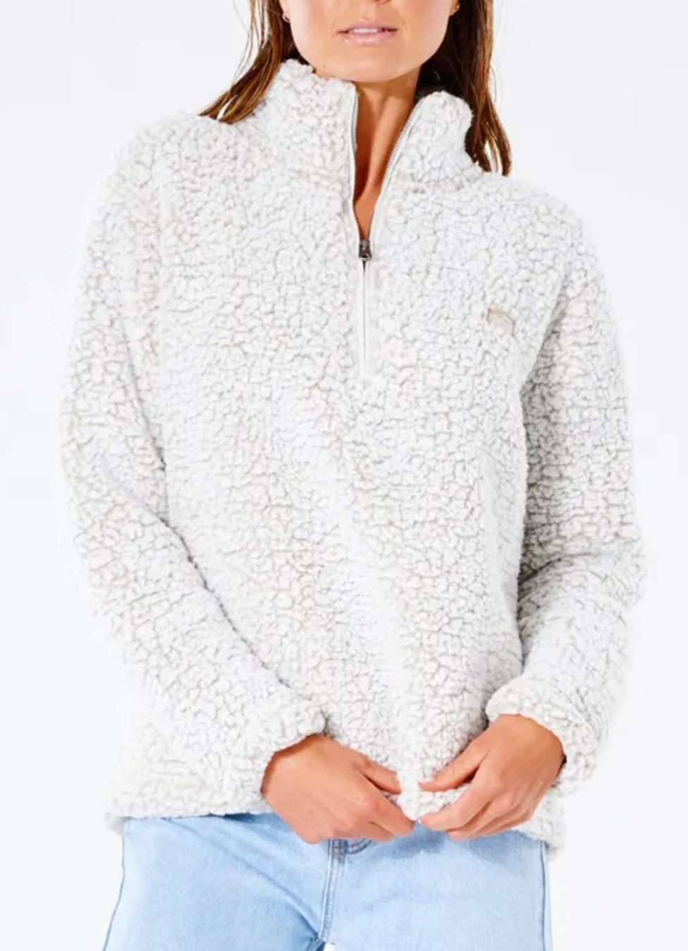 A person with long hair wears the Rip Curl Dark N Stormy 1/4 Zip Crew, a super soft cream-colored fleece jumper featuring a high collar and small logo on the chest, standing against a white background in light blue jeans.