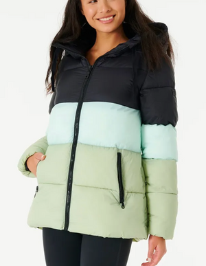 A smiling woman wears a Rip Curl Anti Series Insulated II Jacket featuring color-blocked sections in black, mint green, and light green. This water-repellent puffer has a zipper and front pockets. She pairs it with black pants against a white background.