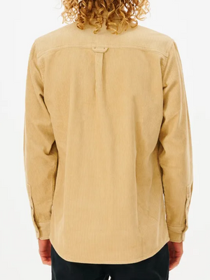Back view of a person with curly hair wearing a Rip Curl State Cord Shirt, featuring long sleeves and buttoned cuffs in light brown cotton corduroy, paired with dark pants. A loop decorates the upper back while their arms hang relaxed at their sides.