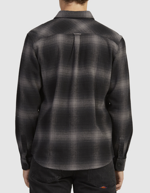 A person is seen from behind wearing the Rip Curl Count Flannel Shirt, showcasing a black and gray plaid pattern made of brushed cotton. The shirt features long sleeves and pairs seamlessly with black pants against a simple light-colored background.