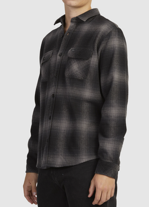 A person is wearing the Rip Curl Count Flannel Shirt, made from brushed cotton in a black and gray plaid with two chest pockets, paired seamlessly with black pants. The face is out of frame, highlighting the chic ensemble.