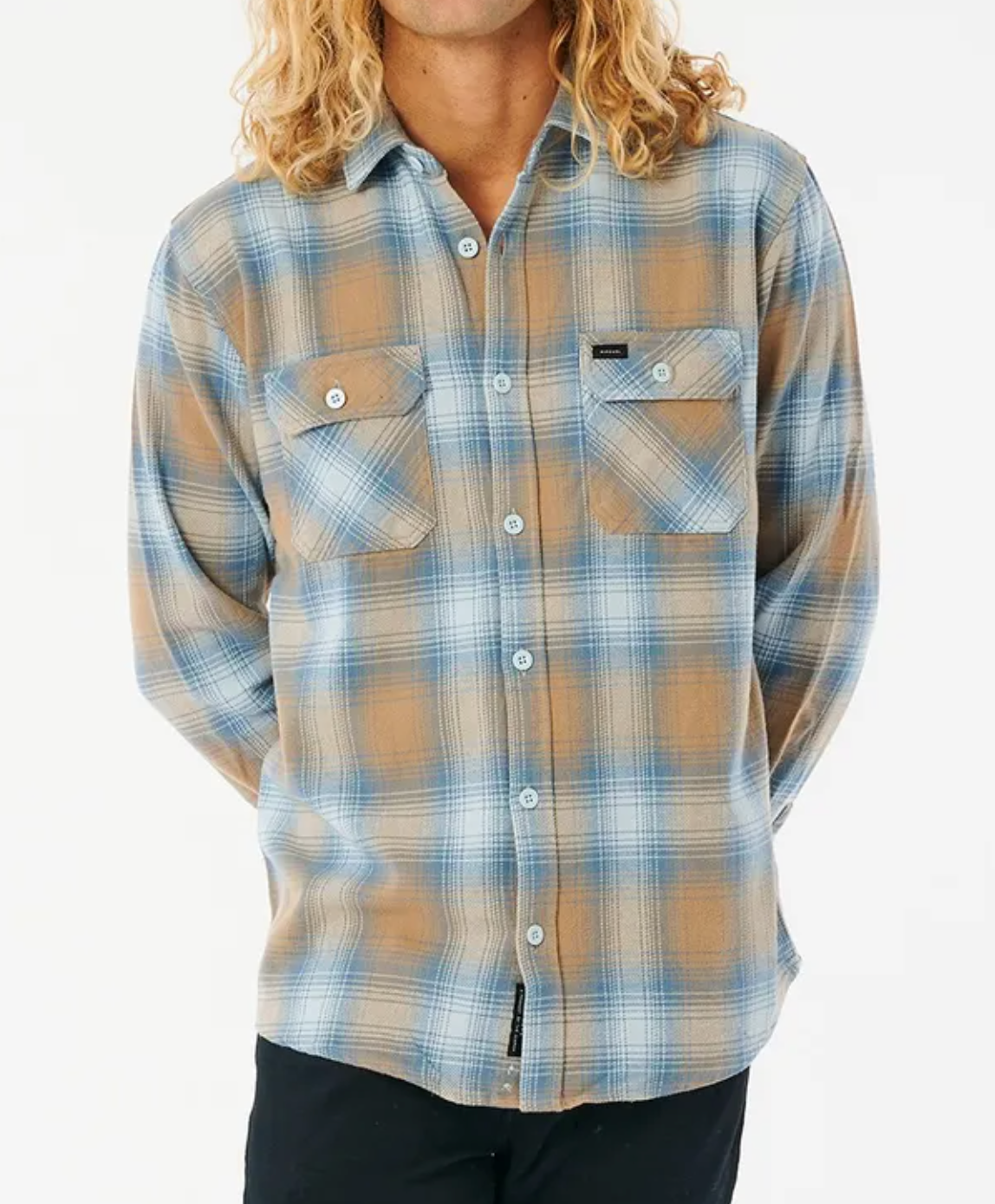 A person with long, wavy blond hair wears a Rip Curl Count Flannel Shirt—relaxed fit, blue and brown plaid with two chest pockets—and black pants, standing against a plain white background.