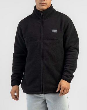 Wearing a black Rip Curl Rincon Zip Crew Polar Fleece with a high collar and small logo on the chest, paired with light blue jeans against a plain, light-colored background.