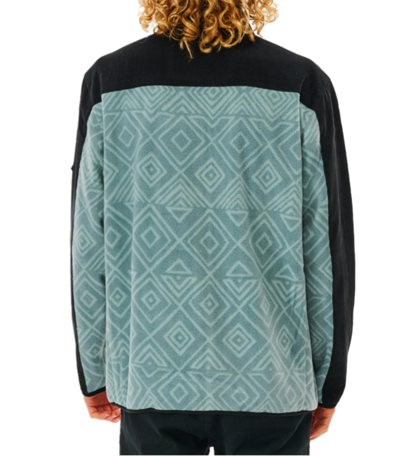 A person with curly hair wears a Rip Curl Anti Series Journey Fleece, featuring a blue and black geometric diamond pattern and solid black shoulders, viewed from the back.