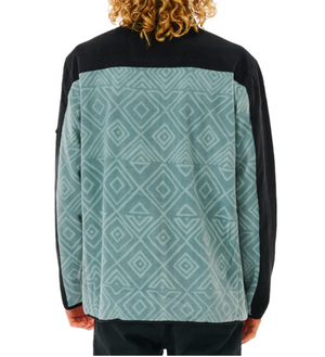 A person with curly hair wears a Rip Curl Anti Series Journey Fleece, featuring a blue and black geometric diamond pattern and solid black shoulders, viewed from the back.
