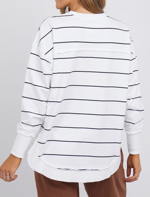 Rear view of a person in a Foxwood Simplified Stripe Crew, a white long-sleeve shirt with black horizontal stripes made from 100% cotton. It offers a relaxed fit and pairs well with brown pants against a plain white background.