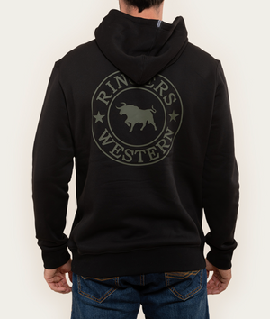 A man stands confidently against a light background, embodying comfort and style in blue jeans and a black Ringers Western Signature Bull Hoodie featuring a bull design on the back.