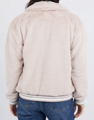 Wearing the Foxwood Nora Bomber, a person is seen from behind in a light pink, soft furry jacket made of 100% Polyester. It has long sleeves and a collar. They paired it with blue jeans against a plain white backdrop.