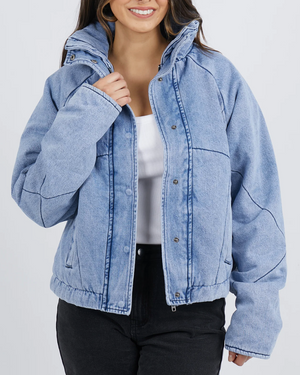 A woman wears a Foxwood Rosalee Denim Jacket over a white top and black pants, smiling warmly. The partially zipped jacket with snap buttons adds a casual yet chic touch to her outfit.
