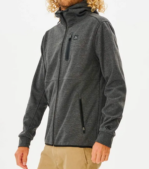 Wearing tan pants, a person is in the Rip Curl Anti Series Departed Zip Thru, a gray hooded jacket known for its durable water-resistant features. Set against a plain white background, it’s the perfect piece of essential winter clothing.