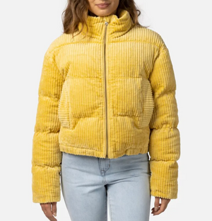 A woman wears the stylish Rip Curl Trippin Cord Jacket in bright yellow with a high collar and front pockets, paired with light blue jeans. The comfortable jacket stands out against the plain white background.