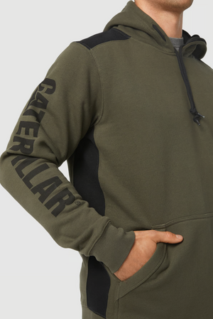 A person wearing a CAT Logo Panel Hooded Sweat in an olive green color with black accents on the shoulder and side. The left sleeve features "CATERPILLAR" printed in prominent black letters along its length. The person stands with a hand in the front pocket, which includes a hidden velcro phone pocket.