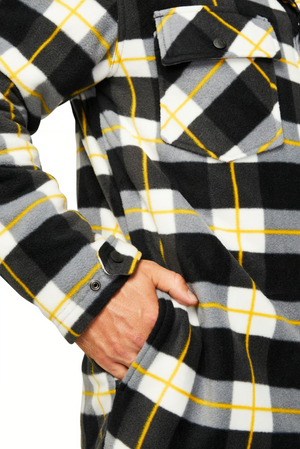 A person wearing the CAT Active Work Jacket in a black, white, gray, and yellow plaid pattern with chest pockets and adjustable cuffs places their right hand in a side pocket. Only their torso and hand are visible.