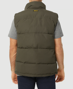 A person in a grey short-sleeve shirt wears a CAT Arctic Zone Vest with an insulated stand-up collar. The olive green vest has a small yellow and black tag at the top, highlighting its sleek design. Their back faces the camera against a plain white background.