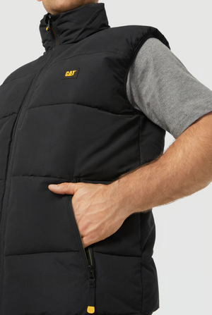 A person wearing a grey short-sleeve shirt layered with a black CAT Arctic Zone Vest featuring an insulated stand-up collar and zippered pocket, shown from shoulders to waist, with their hand partly inside the vest pocket.