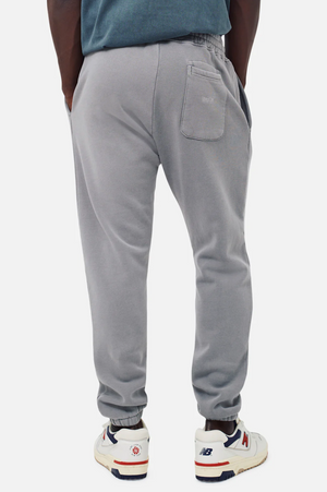 Person wearing Industrie The Del Sur Track Pant in light gray, hands in pockets, shown from behind. These joggers have an elastic waistband and one back pocket. They're paired with New Balance sneakers in white with red and navy accents, creating a casual style ideal for any outing.