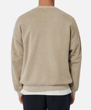 A person is seen from behind, wearing the Industrie The Del Sur Sweat in an oversized beige fit, layered with a white shirt peeking through. Dark pants complete the look against a plain white backdrop.