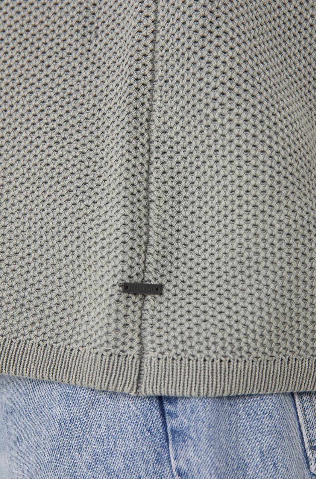 Close-up of Industrie The Washed Culver Knit in light gray waffle texture with a small black rectangular tag near the hem, classic crew neck style, paired with light blue denim jeans.