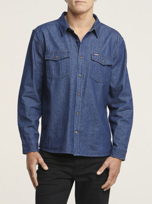 Someone is wearing the Wrangler Roadside Denim Shirt, crafted from 100% cotton in blue, with long sleeves and two chest pockets, paired with black pants against a plain white background.