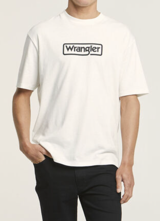 Wearing a Wrangler Border Tee made from 100% cotton with a logo on the chest, this person in a regular fit shirt and dark pants stands against a plain background, one hand in their pocket.