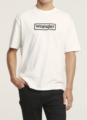 Wearing a Wrangler Border Tee made from 100% cotton with a logo on the chest, this person in a regular fit shirt and dark pants stands against a plain background, one hand in their pocket.
