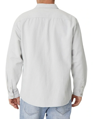 Rear view of a person wearing Industrie The Portland Shirt, a light gray cotton linen long-sleeve button-up overshirt with a relaxed fit, collar, and buttoned cuffs. Paired with light blue jeans against a plain white background.