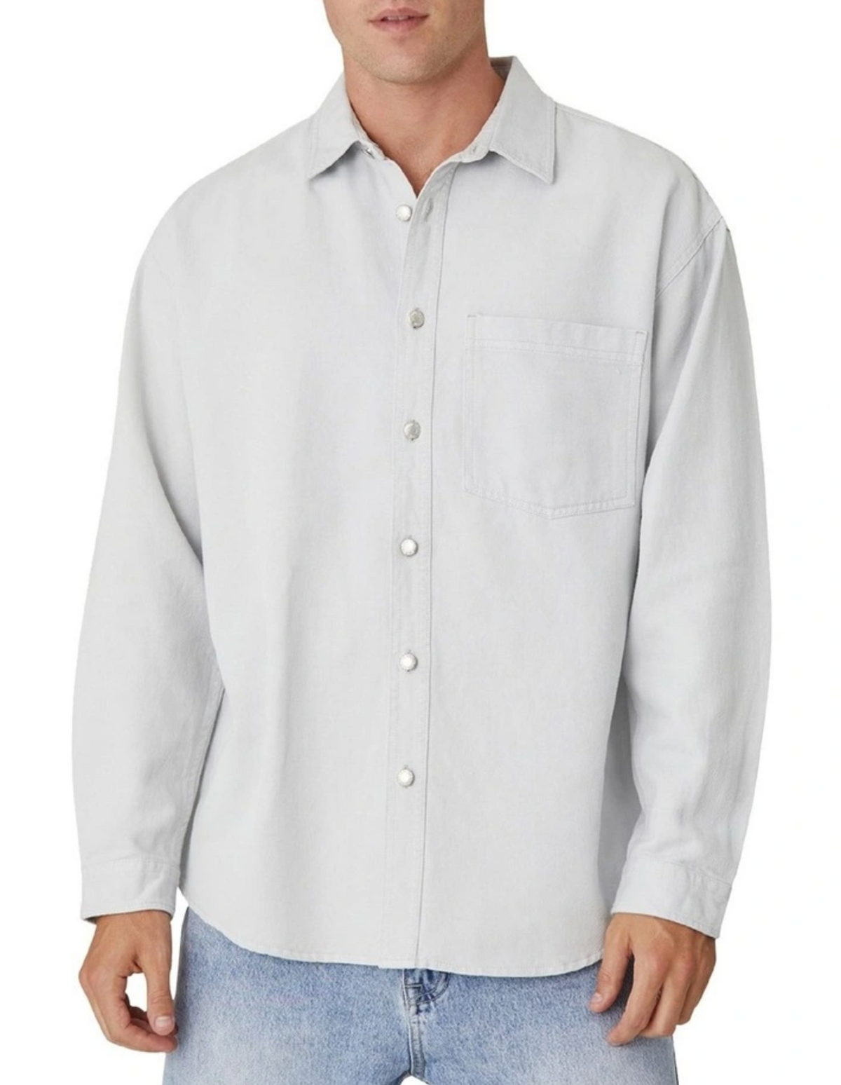A man is wearing Industrie The Portland Shirt, a light gray relaxed-fit overshirt with long sleeves and a chest pocket, paired with light blue jeans. The casually styled cotton-linen shirt complements his laid-back look against a plain white background.