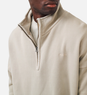 Someone wearing an oversized beige "Industrie The Washed Del Sur Track Top" fleece sweatshirt with a high collar. "L'INFUS PRICE" is embroidered on the left chest, and the plain white background enhances its cozy, acid wash-inspired look.