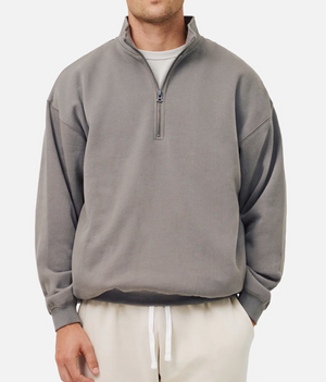 A man wears the gray Industrie The Del Sur Track Top in an oversized fit over a white T-shirt and cream drawstring pants, standing against a plain light background. His face is partially out of frame.