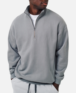 Wearing the Industrie The Del Sur Track Top in light gray, a person enjoys its oversized fit over a white shirt. Their hands are tucked into the pockets of matching comfy sweatpants, while the soft fleece lining enhances coziness against a plain white backdrop.