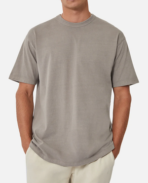 Wearing the Industrie The Del Sur Tee, a plain gray, 100% cotton, short-sleeved shirt with an oversized fit for comfort, a person stands against a white backdrop with their hands in light-colored pants pockets.