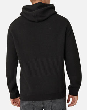 A person wears the Industrie The Robinson Hoodie, featuring a relaxed fit and subtle textured design in black. They pair it with casual gray jeans, standing against a plain white background with their back to the camera.