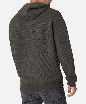 A person is seen from behind wearing the Industrie The Robinson Hoodie in dark gray with a textured herringbone pattern and relaxed fit, paired with slightly faded jeans. They stand against a white background.