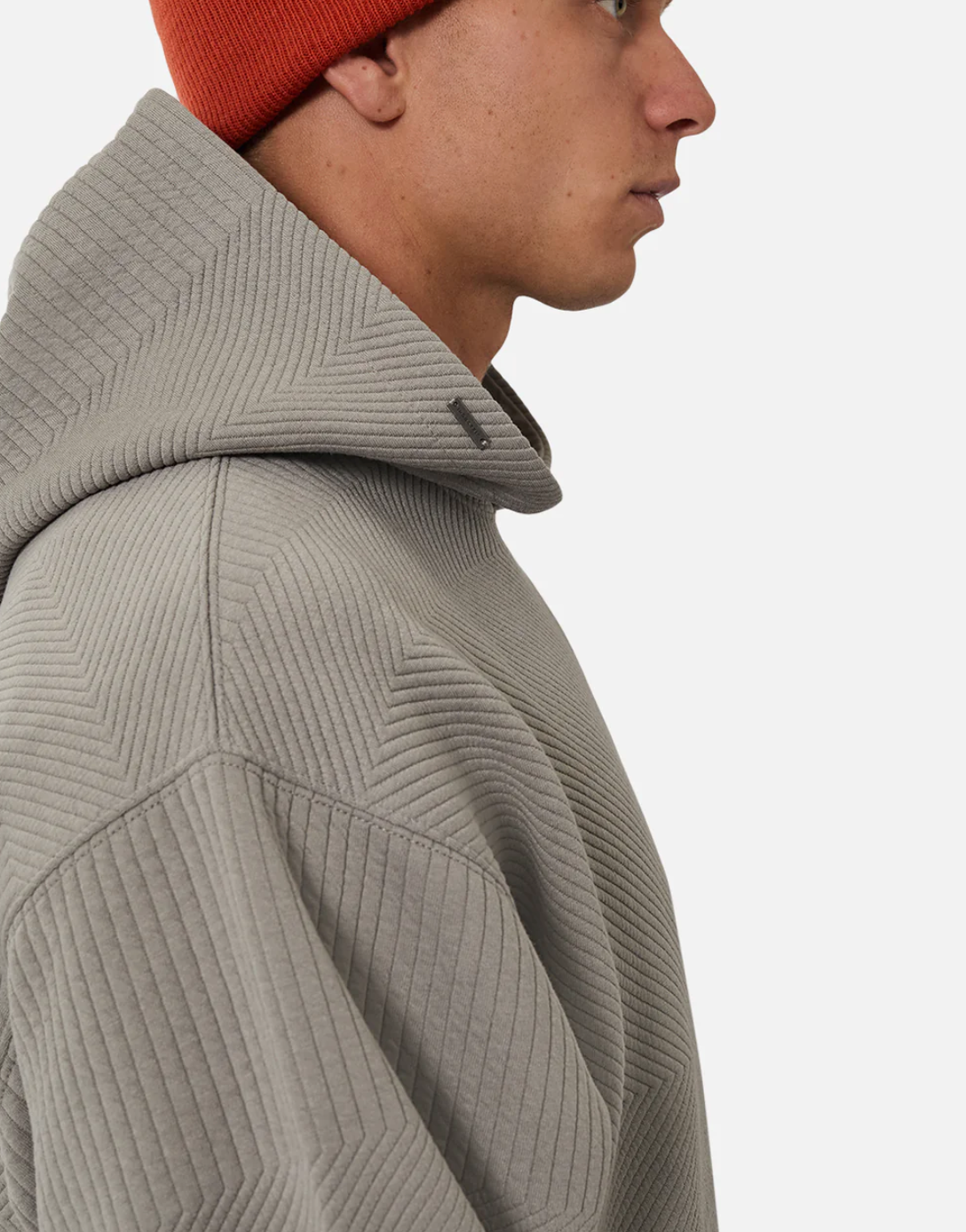 A person in a relaxed fit, textured light gray Industrie The Robinson Hoodie and an orange knit beanie is shown in profile against a plain white background.