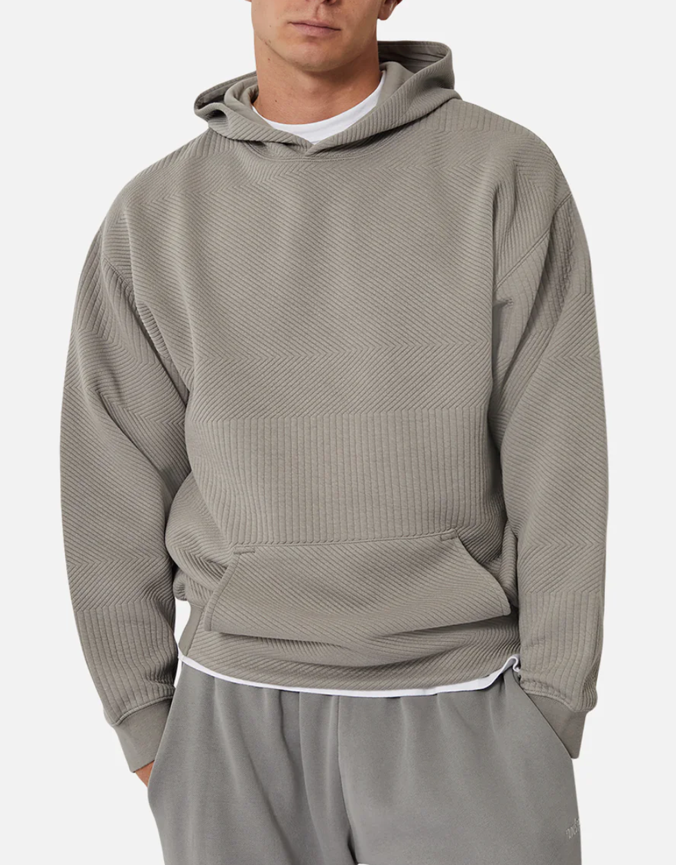 A person wearing Industrie The Robinson Hoodie, a relaxed-fit textured gray hoodie with diagonal patterns and matching pants, stands with one hand in their pocket. A white shirt underneath adds contrast against the plain white background.