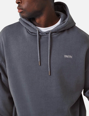 A person wears the Industrie The Del Sur dark gray acid wash hoodie with "INDUSTRIE" on the chest over a white shirt. The comfortable hoodie features drawstrings and an oversized fit as they look to the side against a plain background.