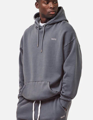 A man is wearing the cozy Industrie The Del Sur Hoodie in dark gray with "INDSTRE" printed on it, matched with oversized jogger pants. His hands are in the pockets as he looks right against a plain light backdrop, nailing the relaxed look.