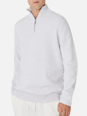 Wearing the Industrie The Lakewood Zip Neck in light gray, a person stands against a white background. The cotton jumper features a high collar and ribbed cuffs, paired with white pants. The face is partially out of frame.